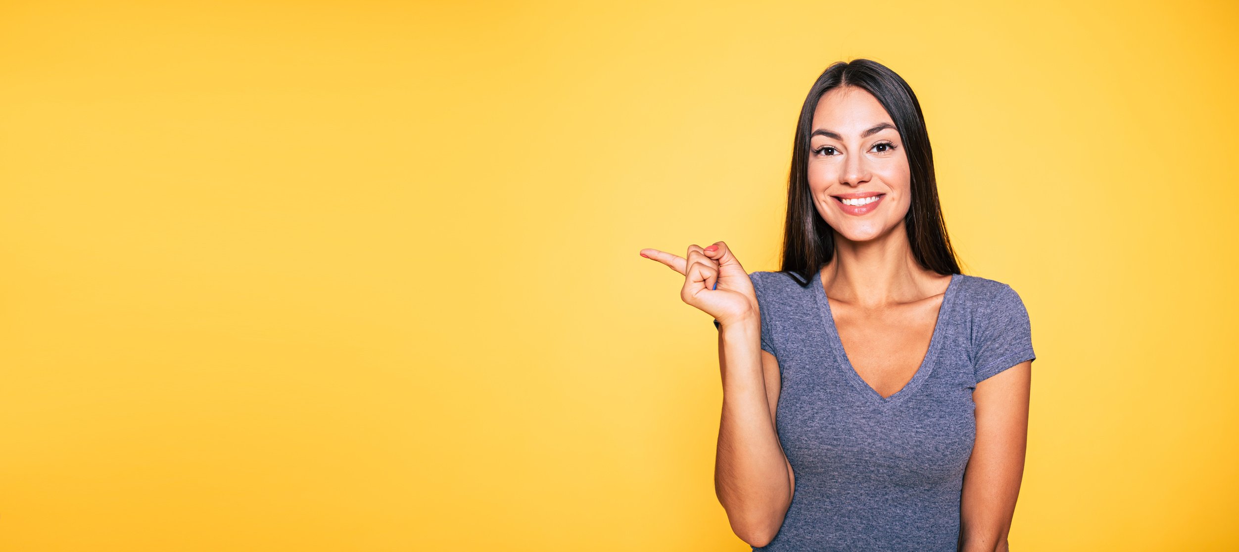 Photo of young excited beautiful happy brunette woman, girl pointing away and smile isolated on yellow background banner